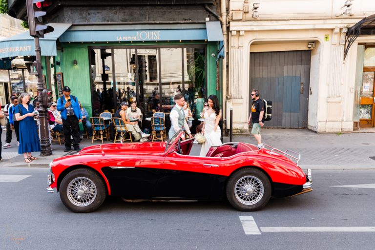 Le marié ouvre la porte d'une Austin Healey cabriolet rouge et noire devant le restaurant "La petite Louise", face à la mairie du 10e à Paris.