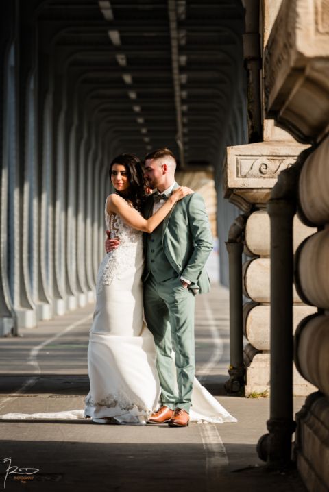 Mariée marocaine éclairée par la lumière naturelle pendant que son mari la regarde tendrement sous le Pont Bir Hakeim à Paris.