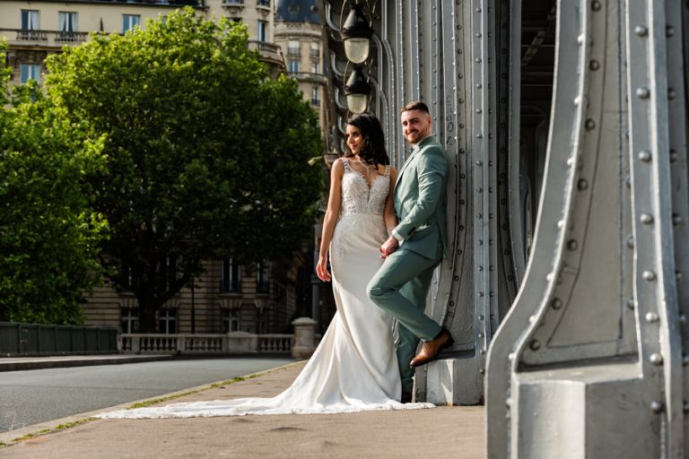 Marié appuyé contre un pilier du Pont Bir Hakeim à Paris, en plan horizontal, sans voiture, avec arrière-plan dégagé grâce à une retouche IA, lors d’un mariage marocain.