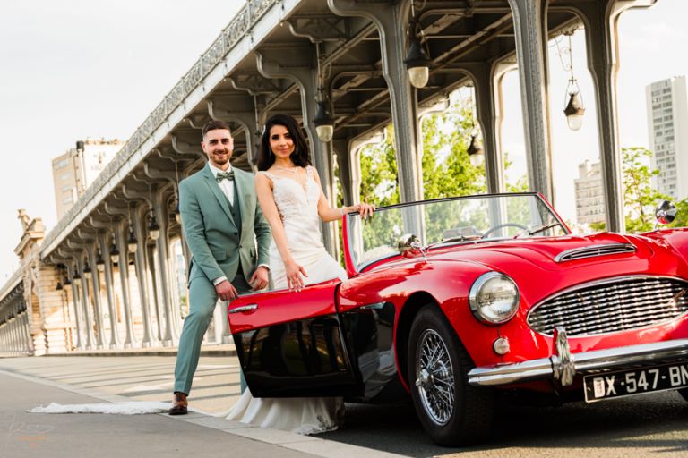 Mariés marocains posant derrière une Austin Healey rouge décapotable, portière ouverte, prise en contre-plongée à Paris.